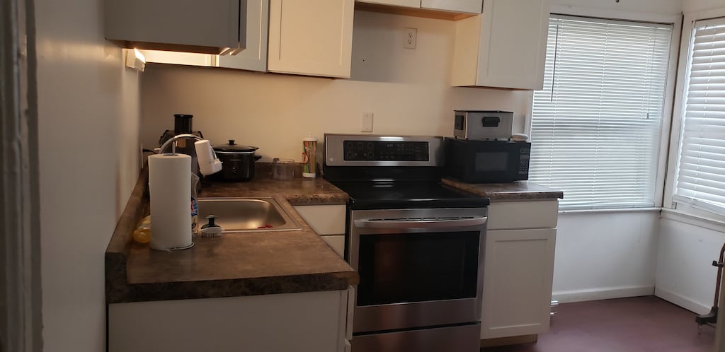 kitchen featuring white cabinets, sink, and stainless steel range with electric cooktop