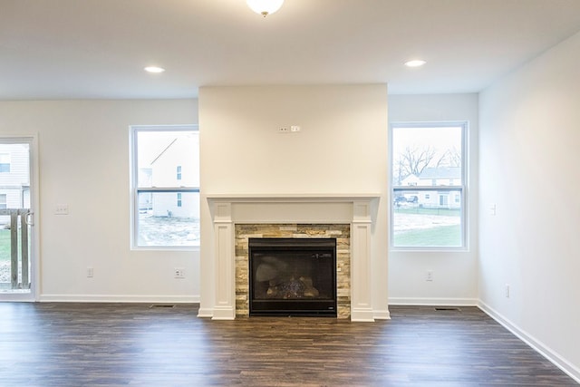 unfurnished living room featuring a stone fireplace, dark hardwood / wood-style flooring, and a healthy amount of sunlight