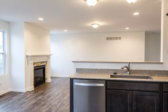 kitchen with a stone fireplace, sink, stainless steel dishwasher, dark hardwood / wood-style floors, and light stone countertops