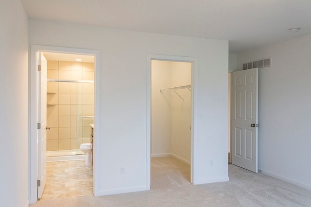 unfurnished bedroom featuring light carpet, ensuite bath, a spacious closet, and a closet