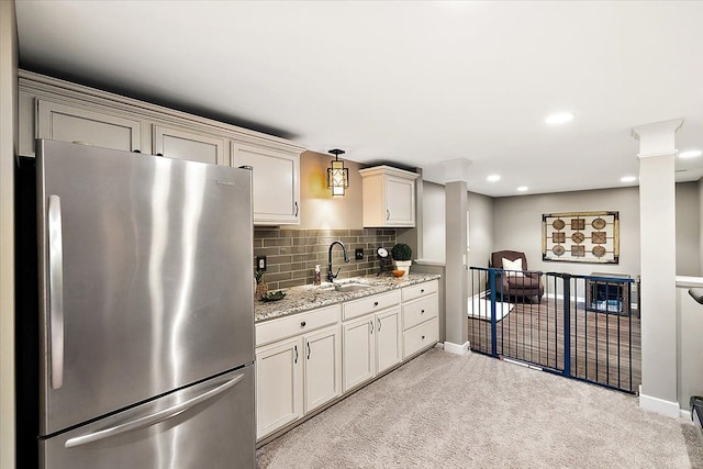 kitchen featuring light stone counters, freestanding refrigerator, a sink, light colored carpet, and backsplash