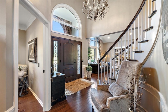 entrance foyer with a towering ceiling, dark wood-type flooring, a notable chandelier, and ornamental molding