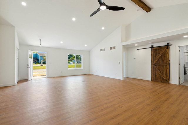 unfurnished living room featuring beamed ceiling, a barn door, high vaulted ceiling, and light hardwood / wood-style flooring