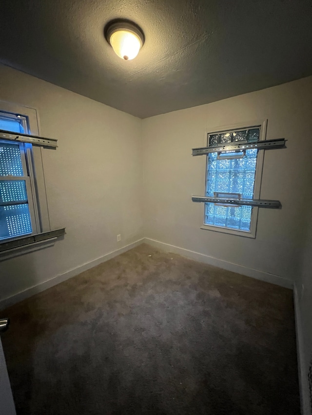 unfurnished room with a textured ceiling and dark colored carpet