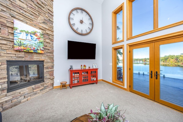 carpeted living room with a stone fireplace, french doors, and a towering ceiling