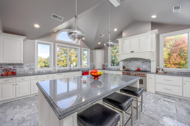 kitchen featuring a kitchen island, range with two ovens, lofted ceiling, and dark stone counters