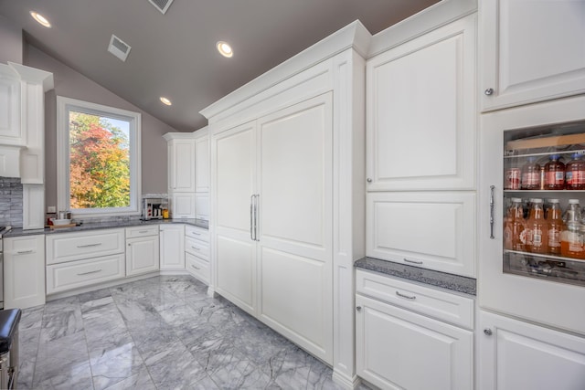 kitchen with decorative backsplash, white cabinetry, dark stone countertops, and lofted ceiling