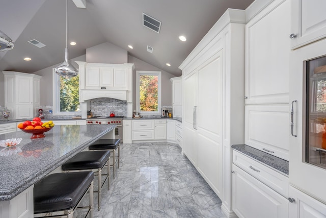 kitchen featuring a kitchen breakfast bar, white cabinets, dark stone counters, and lofted ceiling