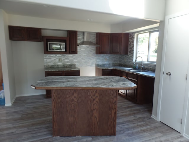 kitchen with sink, wall chimney exhaust hood, a center island, backsplash, and hardwood / wood-style floors