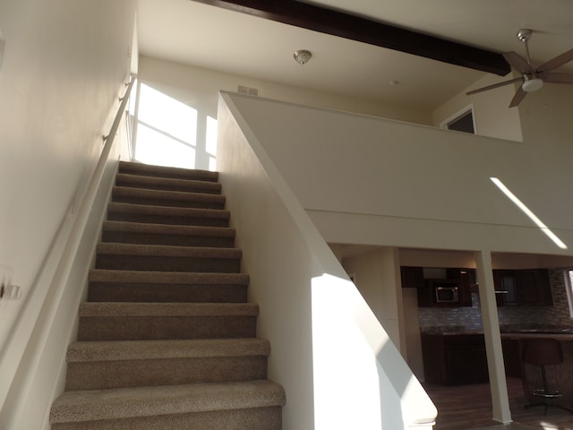 stairway with ceiling fan and vaulted ceiling with beams