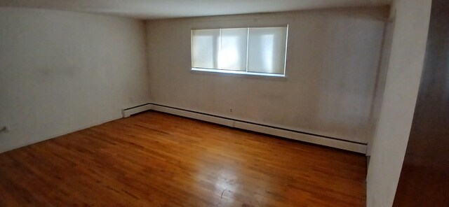 empty room featuring baseboard heating and hardwood / wood-style flooring