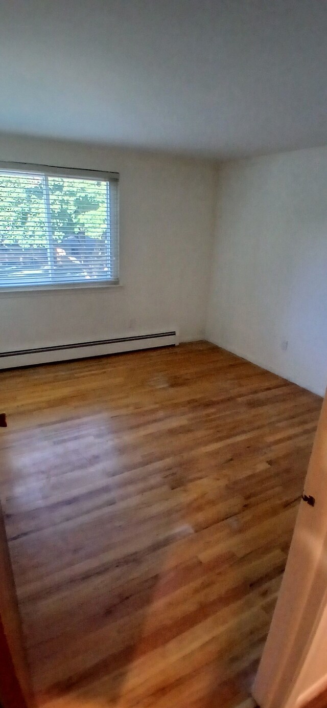 unfurnished room featuring hardwood / wood-style flooring and baseboard heating