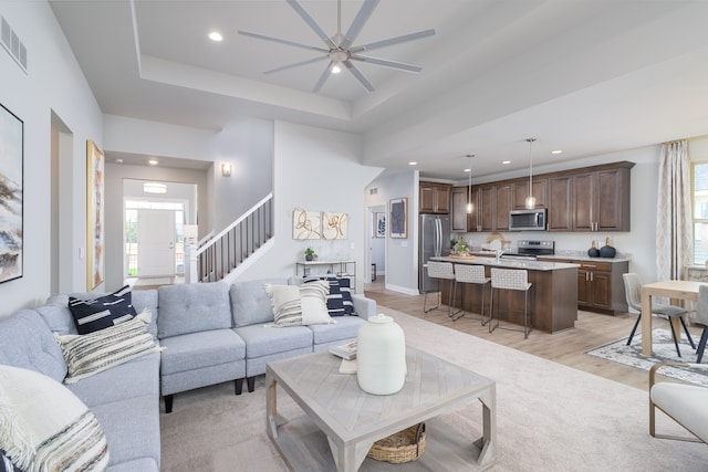 living room featuring light hardwood / wood-style floors, ceiling fan, and a tray ceiling