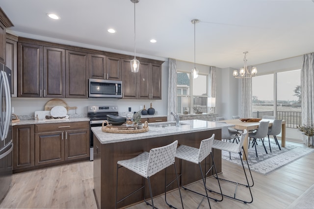 kitchen featuring a kitchen island with sink, light hardwood / wood-style flooring, hanging light fixtures, and appliances with stainless steel finishes