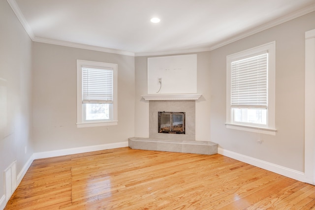 unfurnished living room with a tiled fireplace, plenty of natural light, hardwood / wood-style floors, and ornamental molding