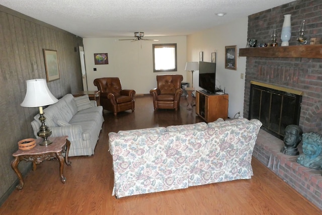 living room featuring a fireplace, ceiling fan, wood-type flooring, and a textured ceiling