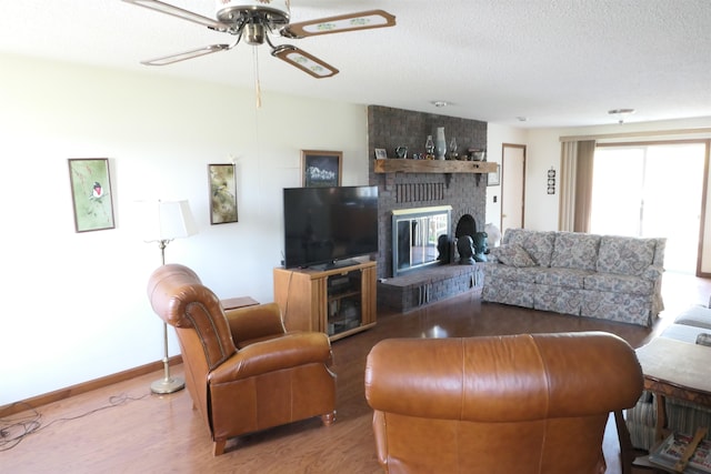 living room featuring ceiling fan, wood-type flooring, a textured ceiling, and a brick fireplace