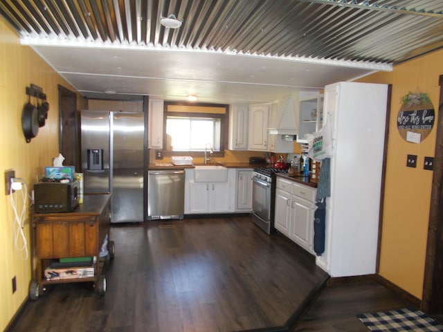 kitchen with appliances with stainless steel finishes, custom range hood, dark wood-type flooring, sink, and white cabinets