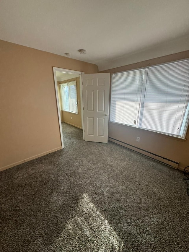 carpeted spare room featuring a healthy amount of sunlight and a baseboard heating unit