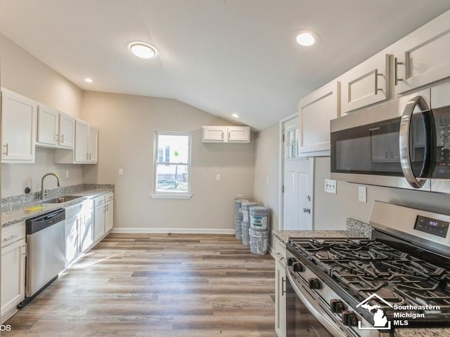 kitchen featuring white cabinetry, sink, light stone countertops, vaulted ceiling, and appliances with stainless steel finishes