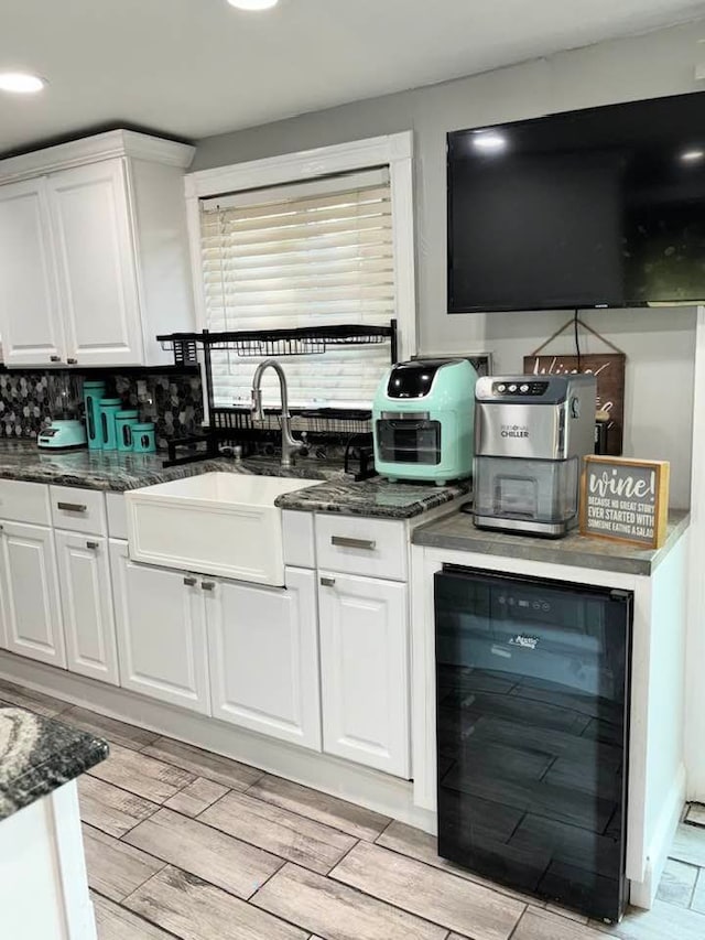 kitchen with sink, beverage cooler, backsplash, dark stone counters, and white cabinets