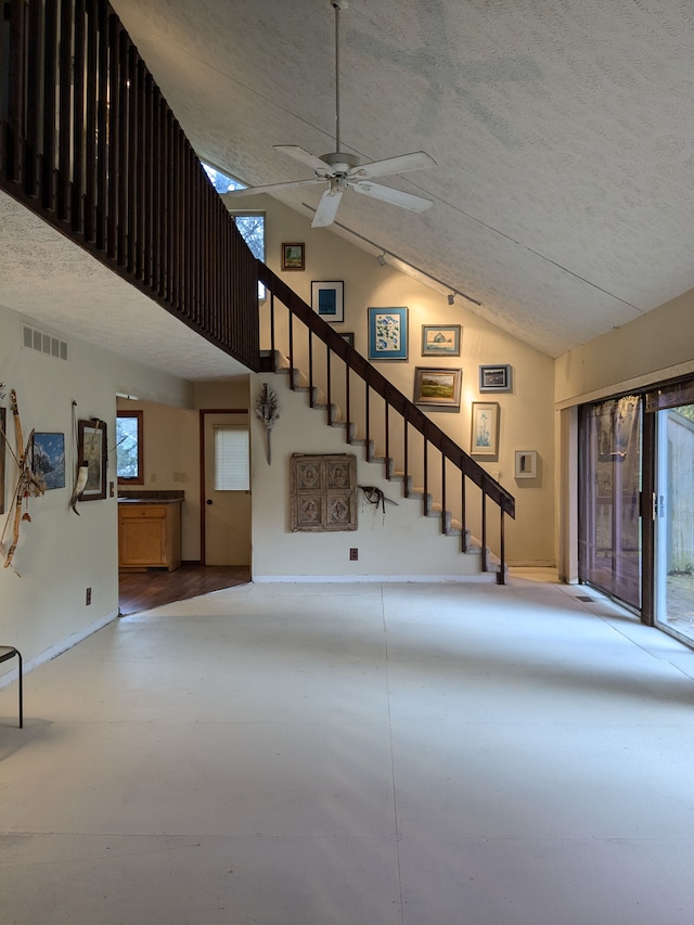 unfurnished living room featuring ceiling fan, a healthy amount of sunlight, a textured ceiling, and vaulted ceiling