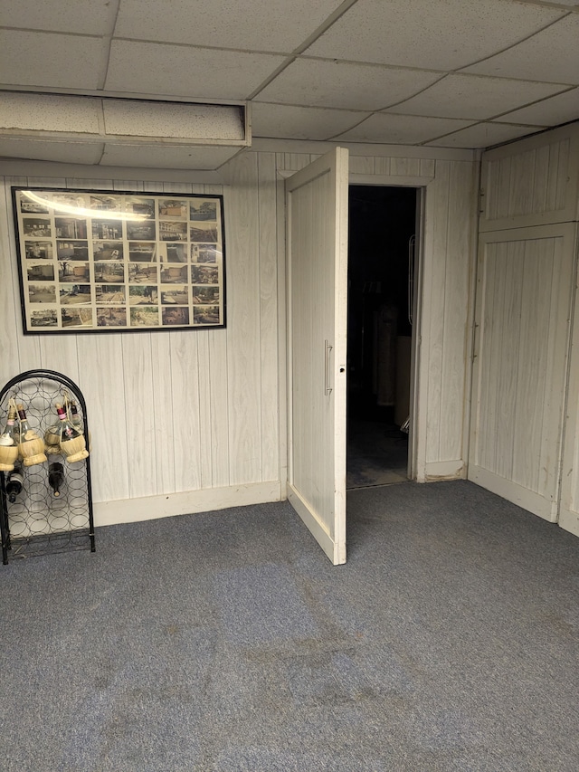 basement with a paneled ceiling, wooden walls, and carpet floors