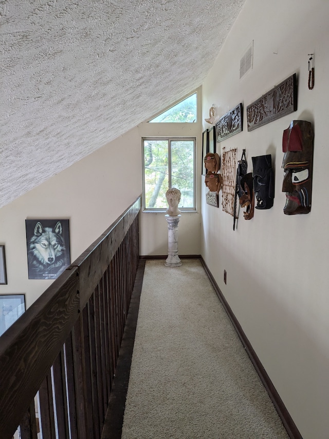 corridor featuring a textured ceiling, carpet floors, and lofted ceiling