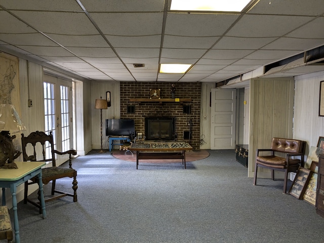 carpeted living room with a paneled ceiling, wood walls, a fireplace, and french doors