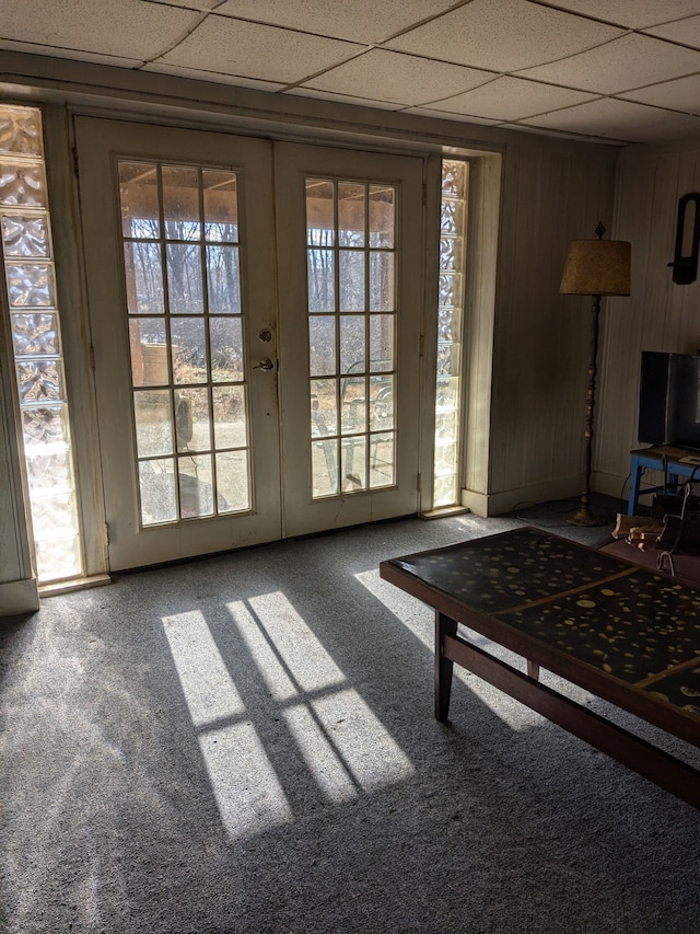 doorway with a wealth of natural light, a drop ceiling, french doors, and wooden walls