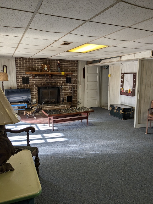 carpeted living room with a brick fireplace, a drop ceiling, and wooden walls