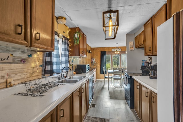 kitchen featuring black range with electric stovetop, sink, white refrigerator, decorative light fixtures, and wooden walls