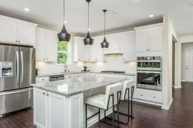 kitchen with white cabinets, hanging light fixtures, a kitchen island, dark hardwood / wood-style flooring, and stainless steel appliances