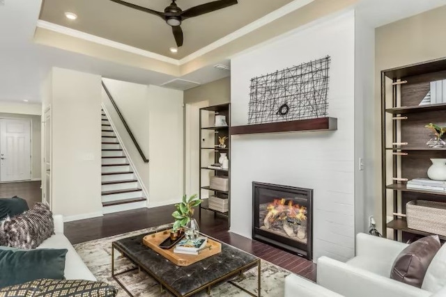 living room with a raised ceiling, ceiling fan, and dark hardwood / wood-style flooring