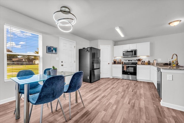 kitchen with white cabinetry, sink, light stone counters, light hardwood / wood-style floors, and black appliances