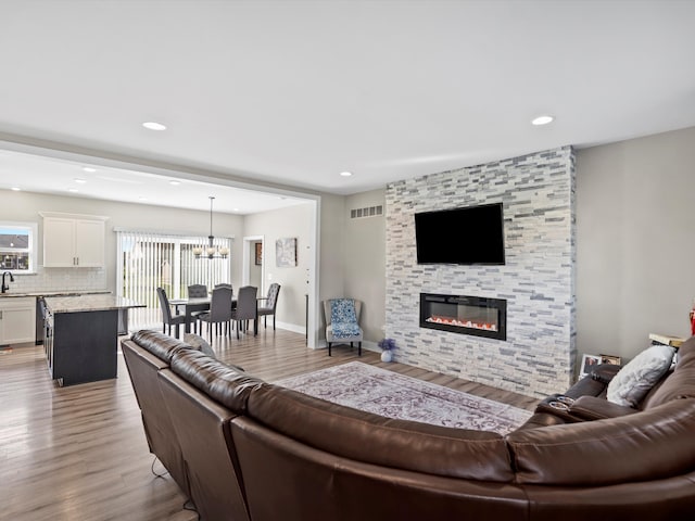 living room with sink, a fireplace, light hardwood / wood-style floors, and an inviting chandelier