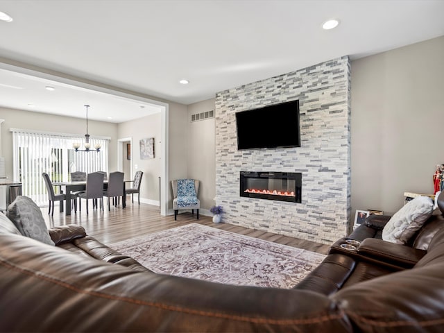 living room with hardwood / wood-style floors, a stone fireplace, and an inviting chandelier