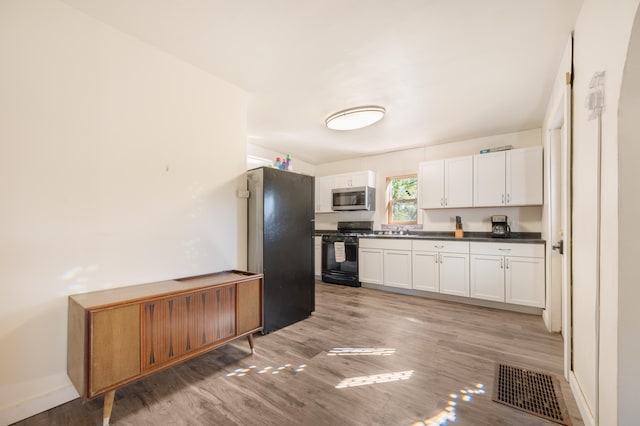 kitchen featuring black appliances, white cabinets, wood-type flooring, and sink