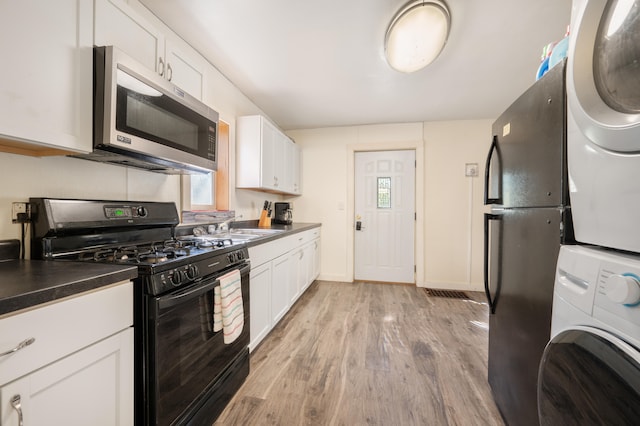 kitchen with plenty of natural light, black range with gas stovetop, white cabinetry, and stacked washer and dryer