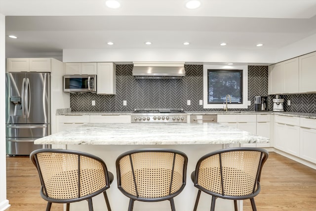 kitchen featuring white cabinets, wall chimney range hood, light wood-type flooring, light stone counters, and stainless steel appliances