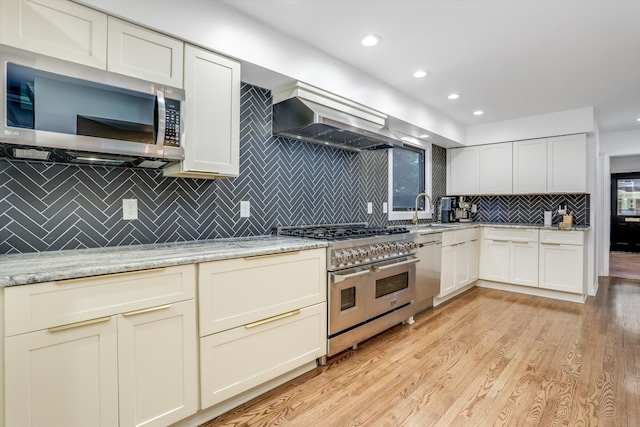 kitchen with backsplash, light stone counters, light hardwood / wood-style floors, and appliances with stainless steel finishes