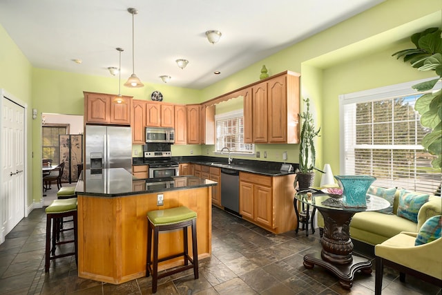 kitchen with appliances with stainless steel finishes, a center island, a healthy amount of sunlight, and pendant lighting