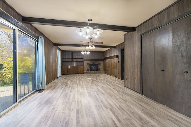 unfurnished living room featuring light hardwood / wood-style flooring, beamed ceiling, wooden walls, a fireplace, and ceiling fan with notable chandelier