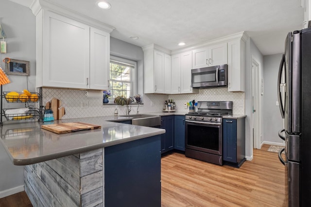 kitchen featuring blue cabinets, white cabinetry, light hardwood / wood-style floors, kitchen peninsula, and stainless steel appliances