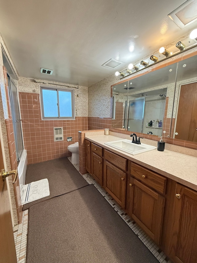 full bathroom featuring combined bath / shower with glass door, vanity, heating unit, tile walls, and toilet