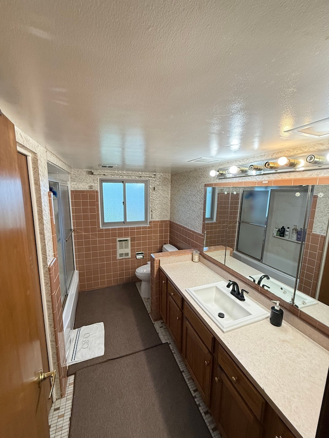 full bathroom with vanity, toilet, enclosed tub / shower combo, a textured ceiling, and tile walls