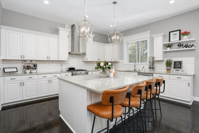 kitchen with a kitchen island, stainless steel appliances, white cabinetry, and wall chimney exhaust hood