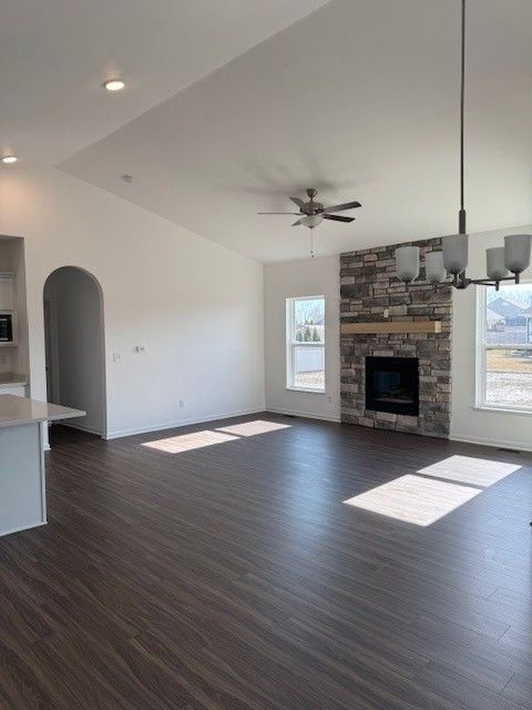 unfurnished living room with arched walkways, dark wood-style flooring, a fireplace, and ceiling fan