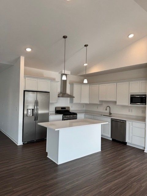 kitchen with stainless steel appliances, wall chimney range hood, a sink, and white cabinets