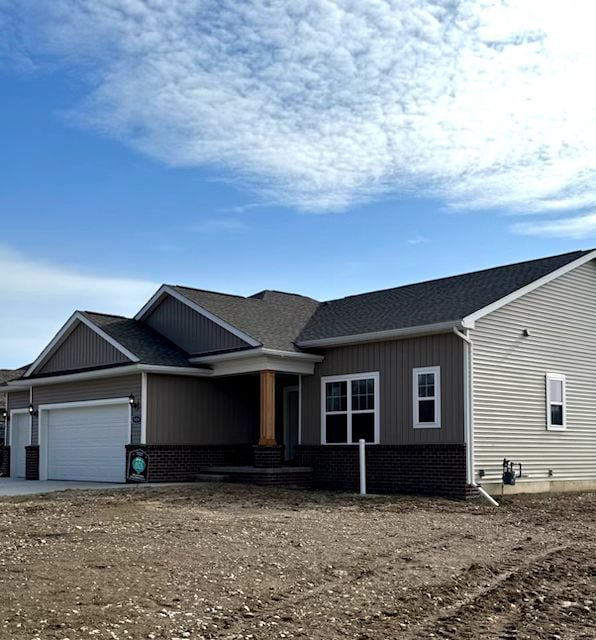 view of front of home featuring a garage, brick siding, and roof with shingles